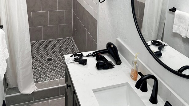 Ein modernes Badezimmer mit Dusche, Waschbecken und einem großen Spiegel.