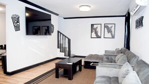 A modern living room with a grey sofa, a black coffee table, and a staircase with a black railing. - Houston Home by NRG Stadium & Downtown (Houston)