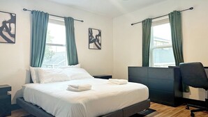 A modern hotel room with a bed, a desk, and two windows with curtains. - Houston Home by NRG Stadium & Downtown (Houston)