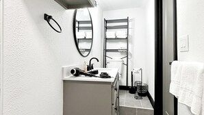 Ein kleines Badezimmer mit integriertem Waschbecken, einem Spiegel, einem Handtuchhalter und einem Regal mit gefalteten Handtüchern.