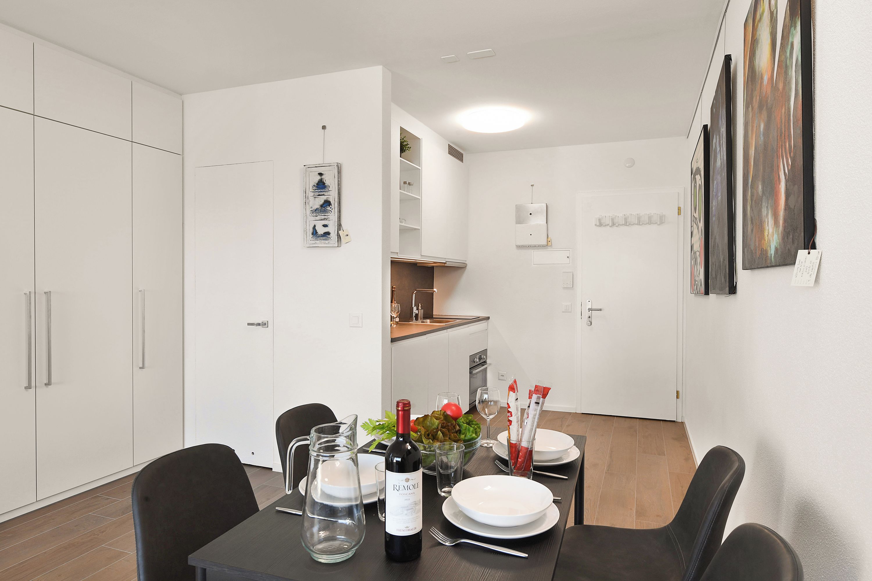 A dining area with a table set for two, a wine bottle, and a bowl of salad.