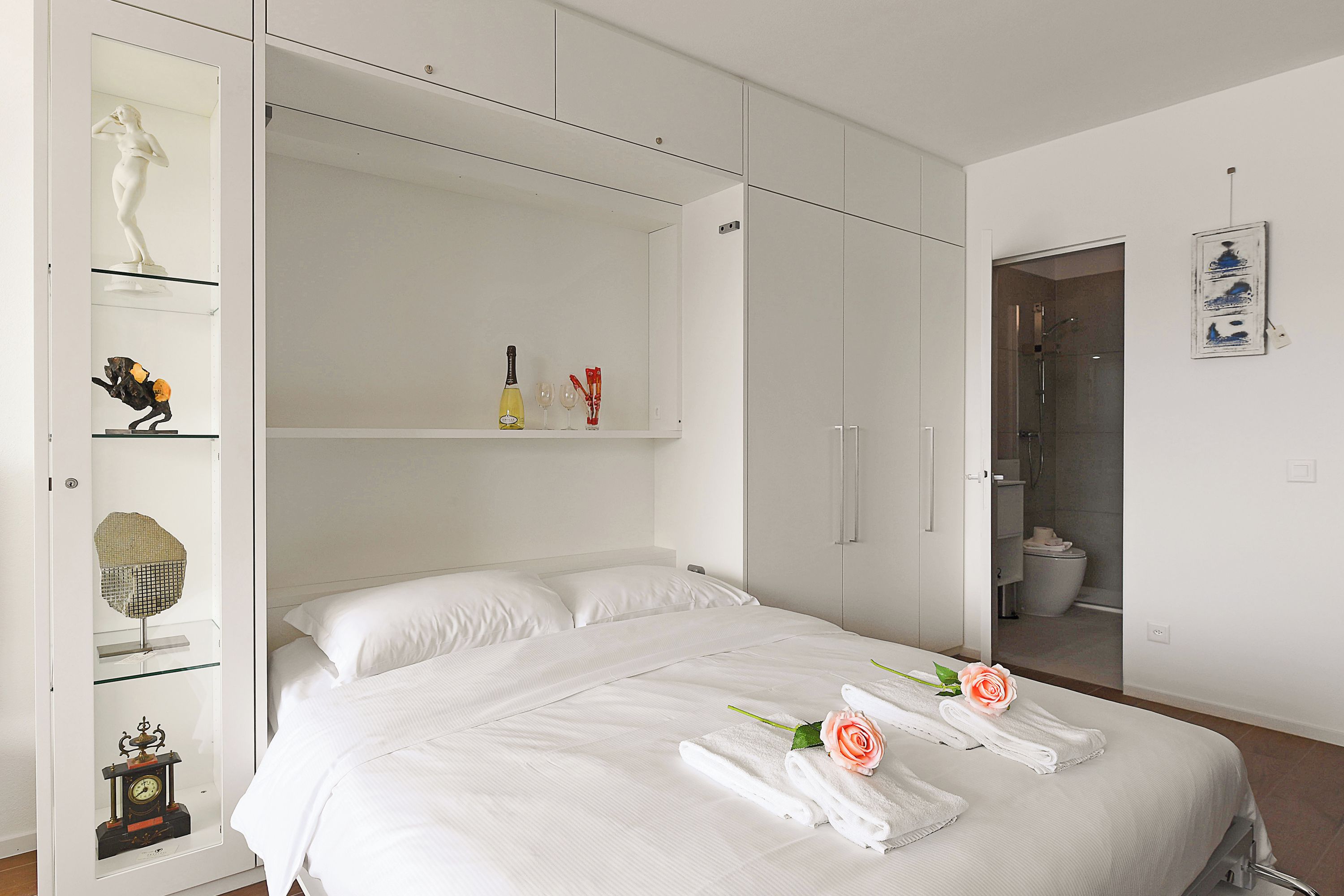 Une chambre d’hôtel moderne avec un grand lit, une armoire aux portes vitrées et une salle de bain visible à travers une porte ouverte.