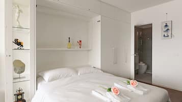 Une chambre d’hôtel moderne avec un grand lit, une armoire aux portes vitrées et une salle de bain visible à travers une porte ouverte.