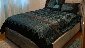 Ein Schlafzimmer mit einer gesteppten Kopfstütze, einer gemusterten Bettdecke und einem blauen Teppich.