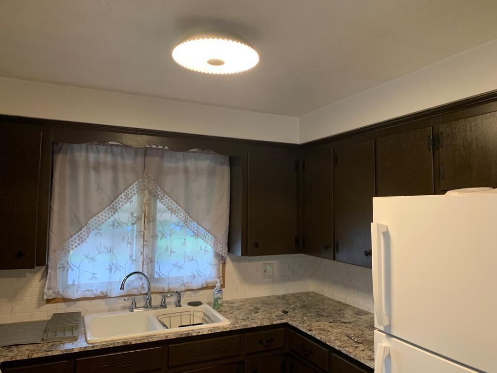 A kitchen with a sink, a refrigerator, and dark wooden cabinets.