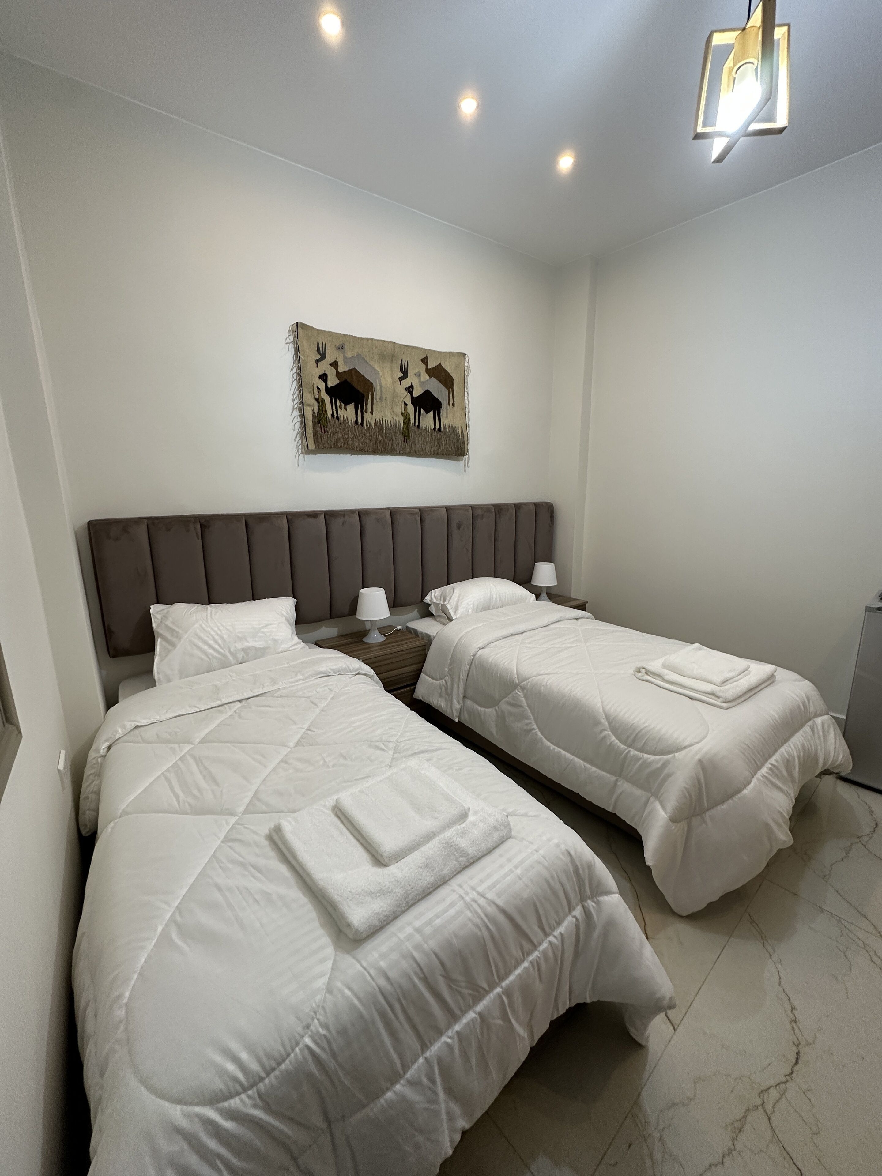 A hotel room with two beds, a headboard, a wall-mounted artwork, and a ceiling light fixture.