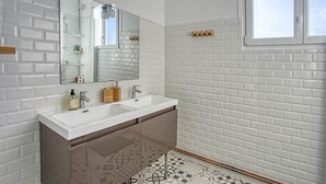 Une salle de bain moderne avec des murs recouverts de carreaux de métro blancs, un meuble-lavabo à deux vasques et un sol à motifs.