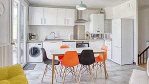 Une cuisine compacte avec des meubles blancs, un lave-linge, une table à manger avec quatre chaises et un four à micro-ondes.