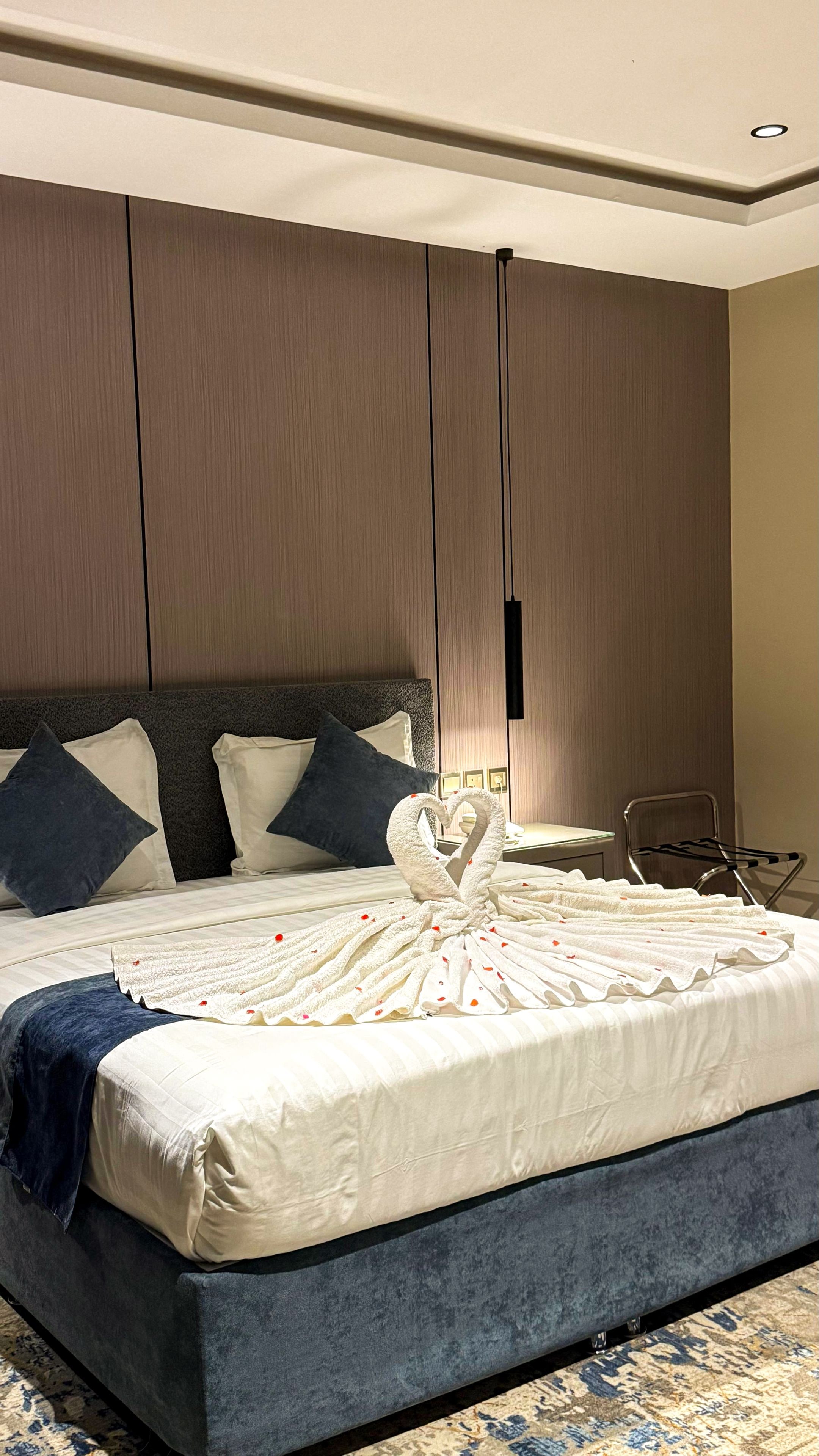 A hotel room with a large bed, a headboard, a wall-mounted light, and a chair.