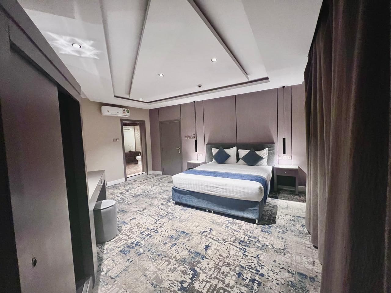 A modern hotel room with a large bed, a bedside table, a nightstand, and a ceiling light fixture.