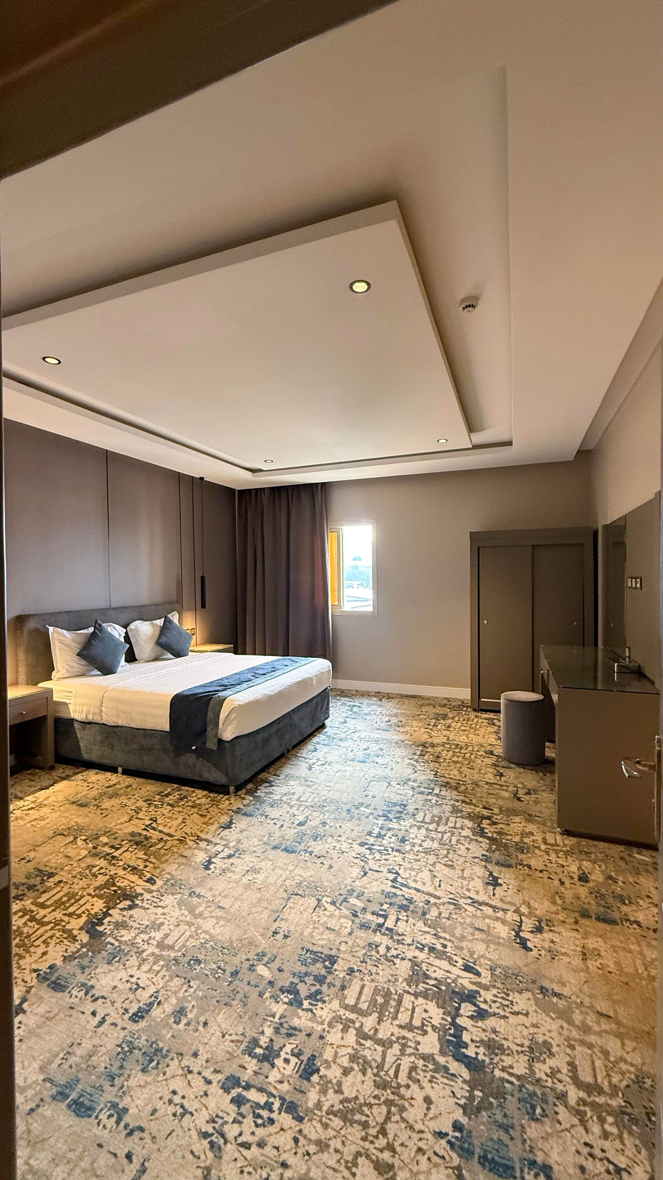 Una habitación de hotel moderna con una cama grande, un escritorio, un armario y un amplio ventanal.