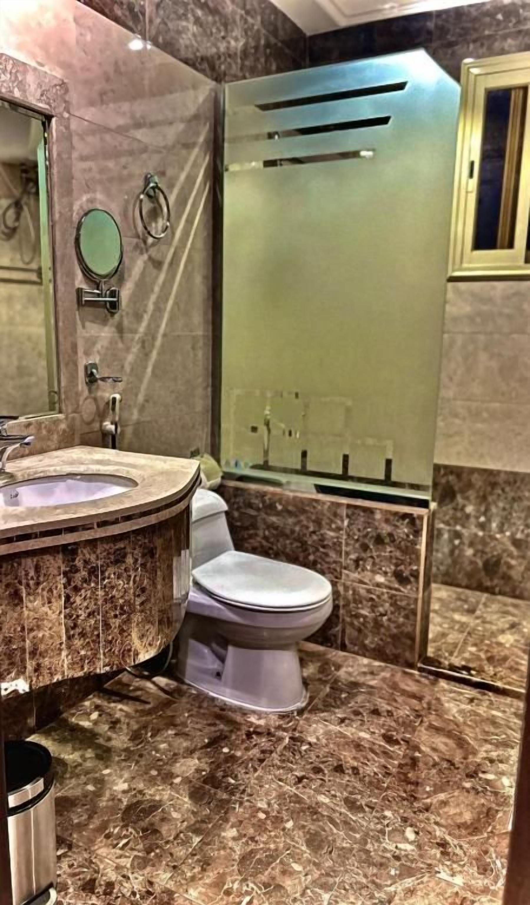 A bathroom with a marble floor, a toilet, a sink with a circular basin, and a mirror.
