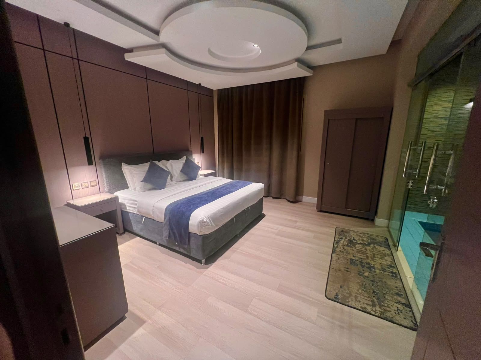 Une chambre d’hôtel moderne dotée d’un grand lit, d’une armoire, d’un bureau et d’une salle de bain avec une douche en verre.