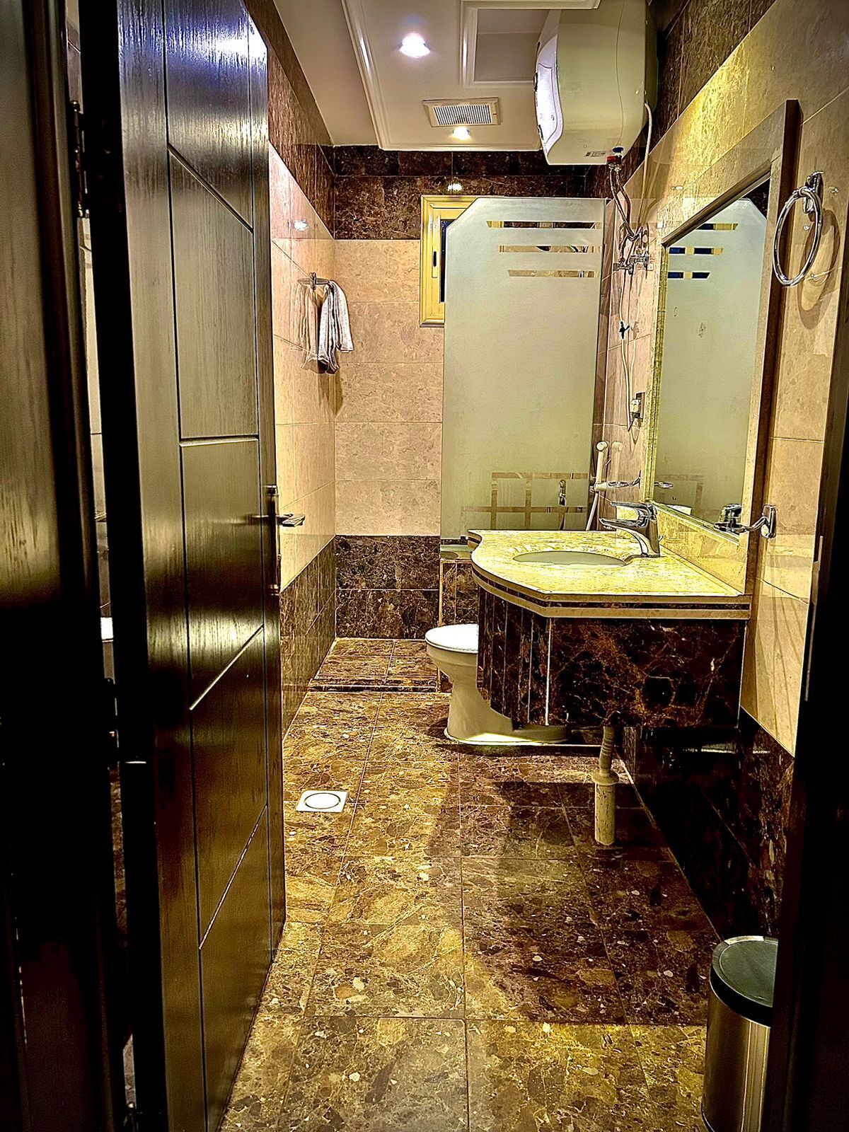 A bathroom with a marble floor, a sink, a toilet, and a mirror.