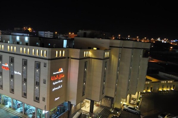 Un edificio de varios pisos con letreros iluminados, una entrada visible y un área de estacionamiento.