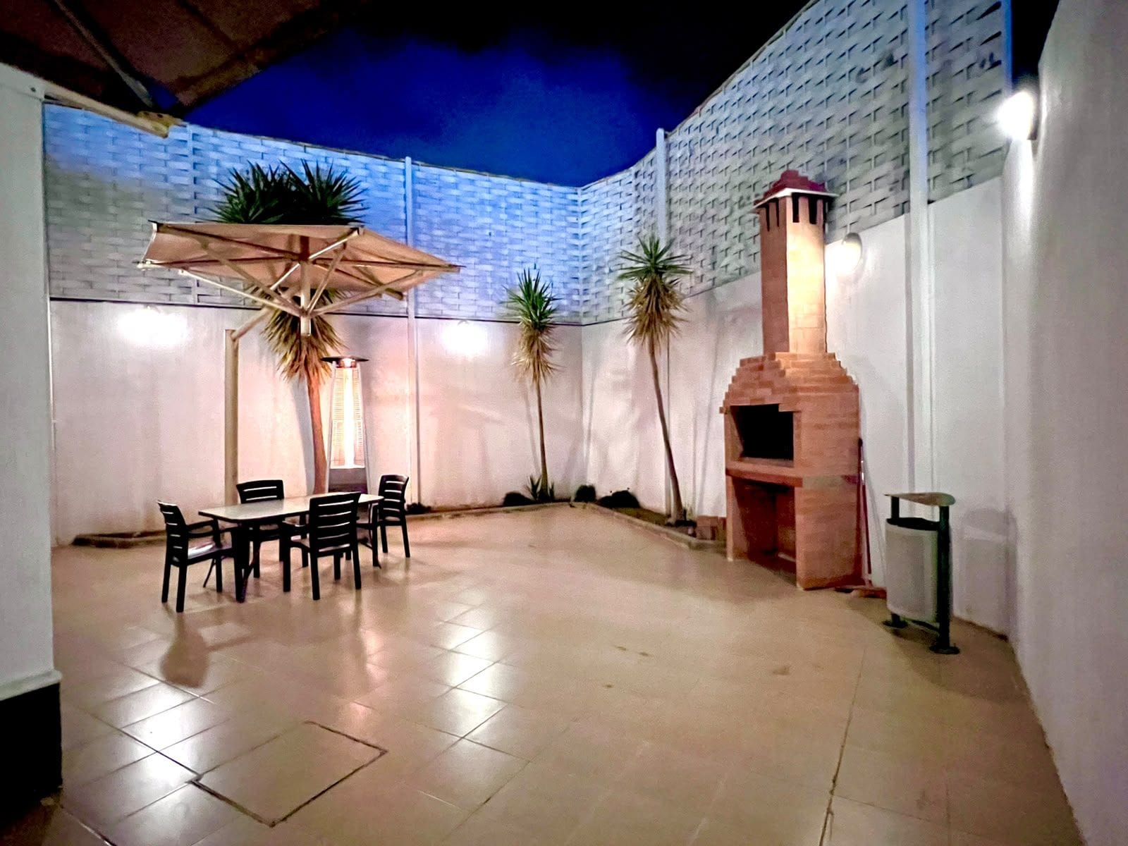 An outdoor patio area with a table and chairs, a brick oven, and potted plants.