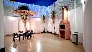 An outdoor patio area with a table and chairs, a brick oven, and potted plants.