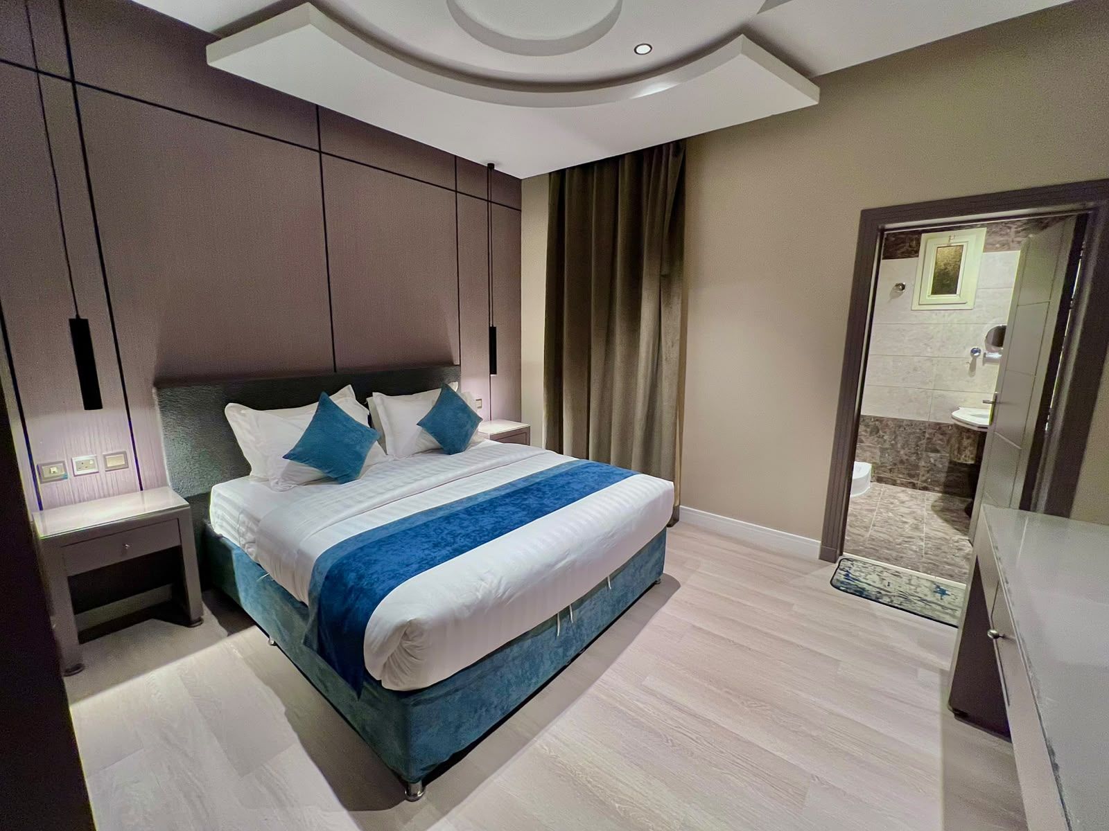 A modern hotel room with a large bed, a nightstand, a mirror, and a view of the bathroom.
