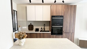 A modern kitchen with a light-colored table, wooden cabinets, a built-in oven, and a vase with dried flowers on the counter.