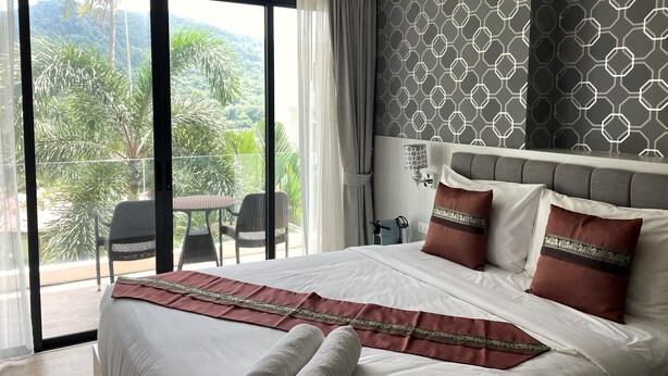 Une chambre d’hôtel avec un grand lit, un balcon doté d’une table et de chaises, et une vue sur la verdure.