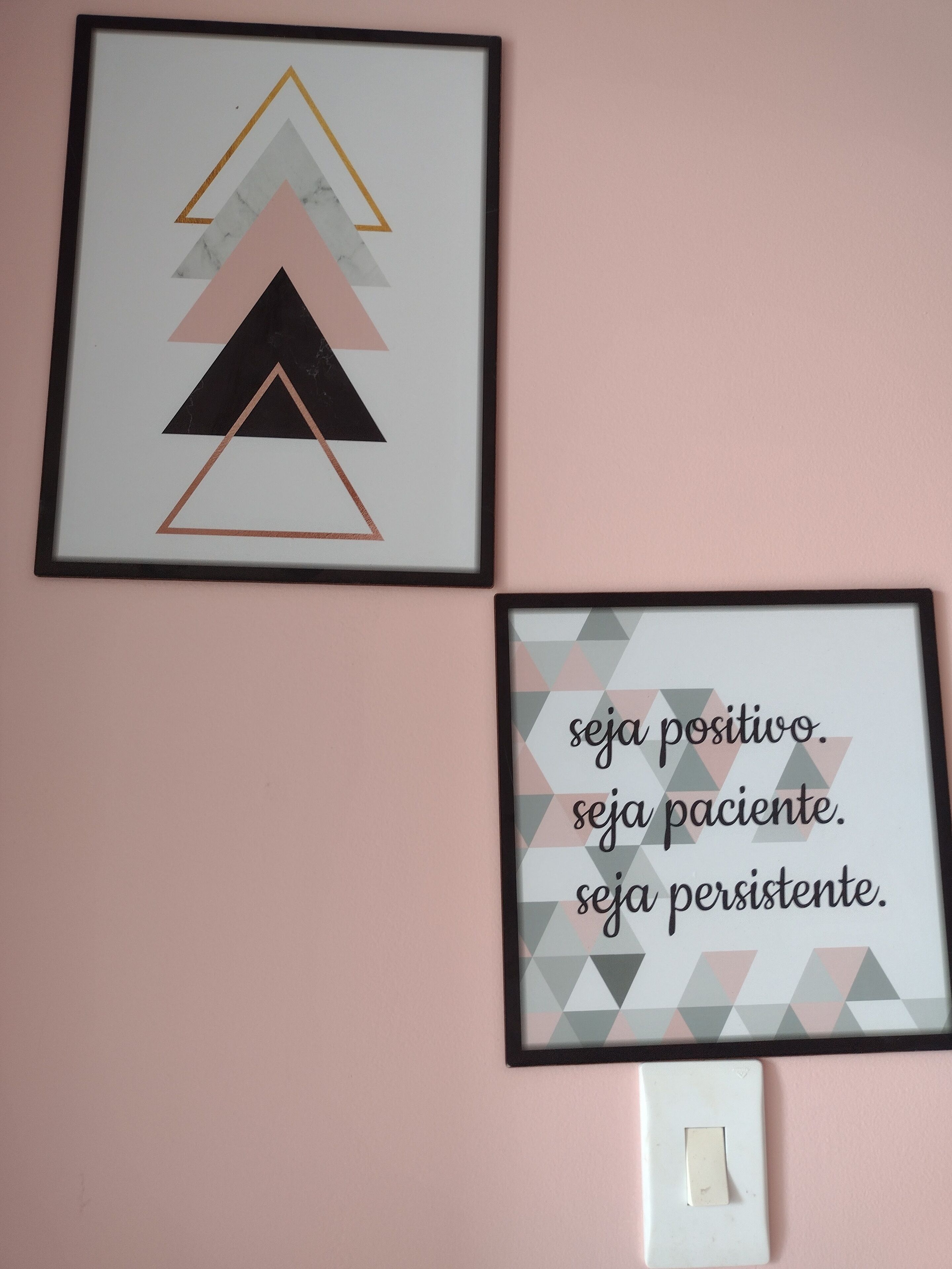 Två inramade konstverk på en rosa vägg, det ena med geometriska former och det andra med ett motiverande budskap.