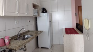 A compact kitchen with white cabinets, a granite countertop, a white refrigerator, and a red rug. - Rua Maria Tognini 296 (Praia Grande)