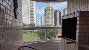 A balcony with a TV, wicker chairs, and a view of tall buildings. - Rua Maria Tognini 296 (Praia Grande)