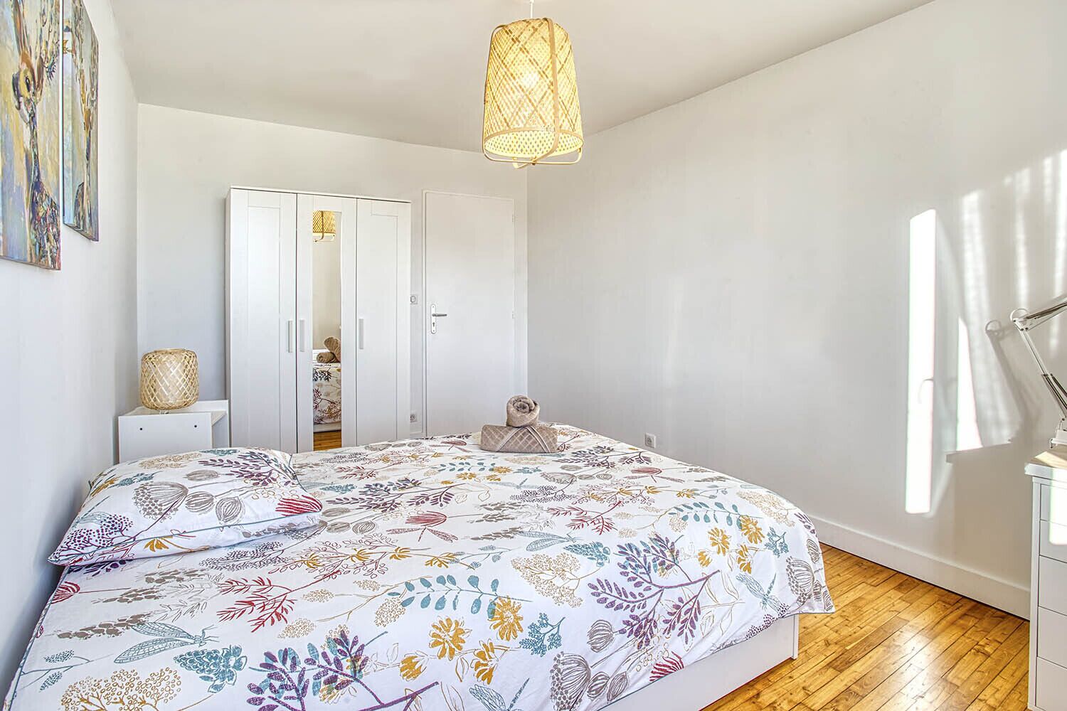 A bedroom with a large bed, a wardrobe, a bedside table with a lamp, and a hanging light fixture.