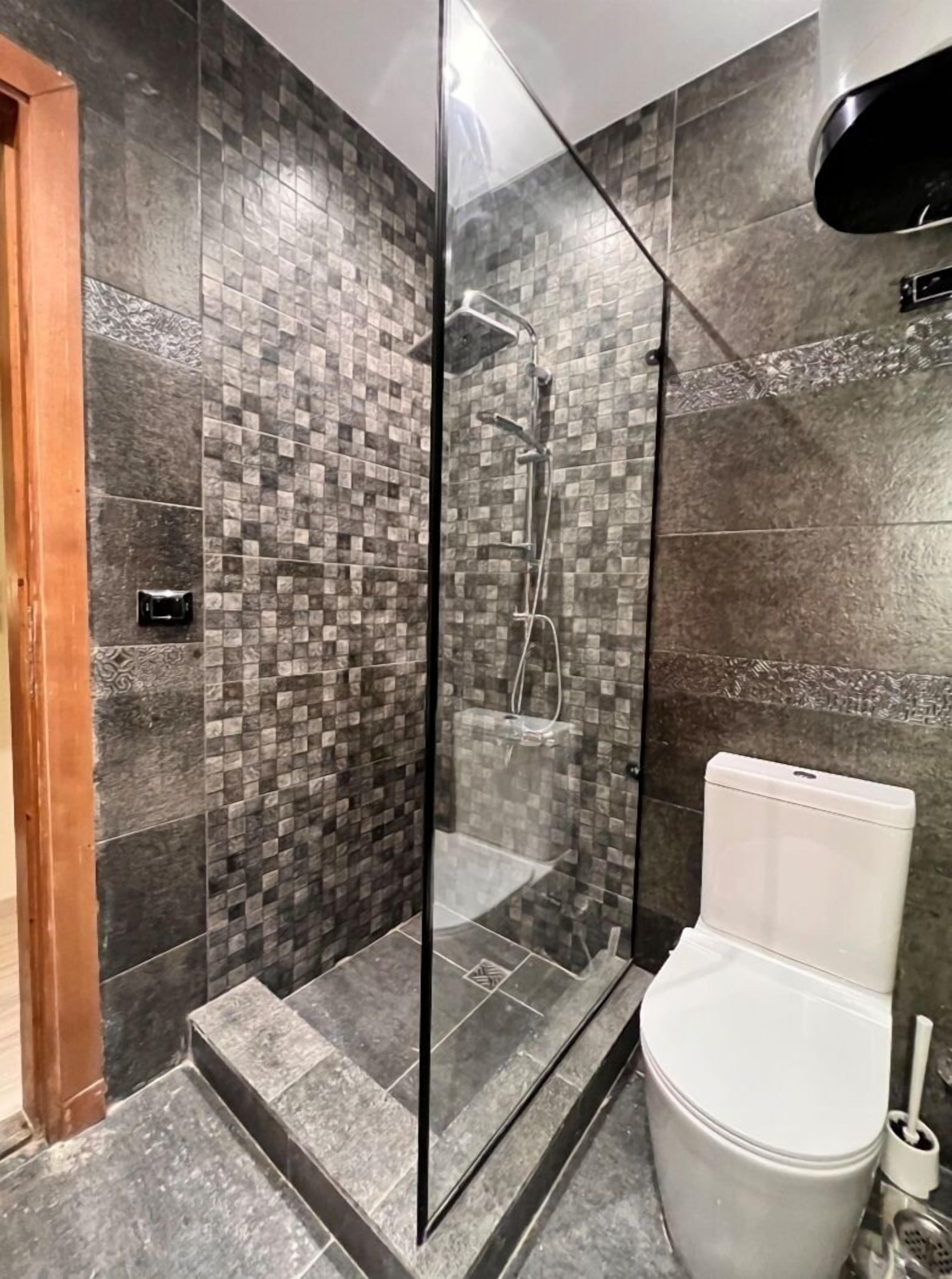 Ein modernes Badezimmer mit einer Duschkabine aus Glas, einer weißen Toilette und einer gefliesten Wand mit einem Schachbrettmuster.