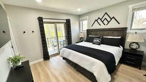 A bedroom with a bed, a nightstand, a lamp, a window, and a view of the outdoors.
