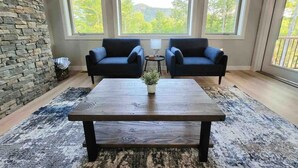 A room with a stone wall, two dark sofas, a wooden coffee table, and large windows overlooking greenery.