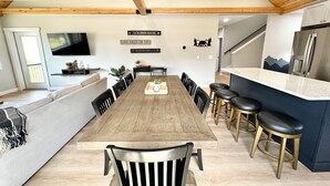 A modern kitchen with a wooden ceiling, a dining area with a long table and chairs, and a bar area with stools.