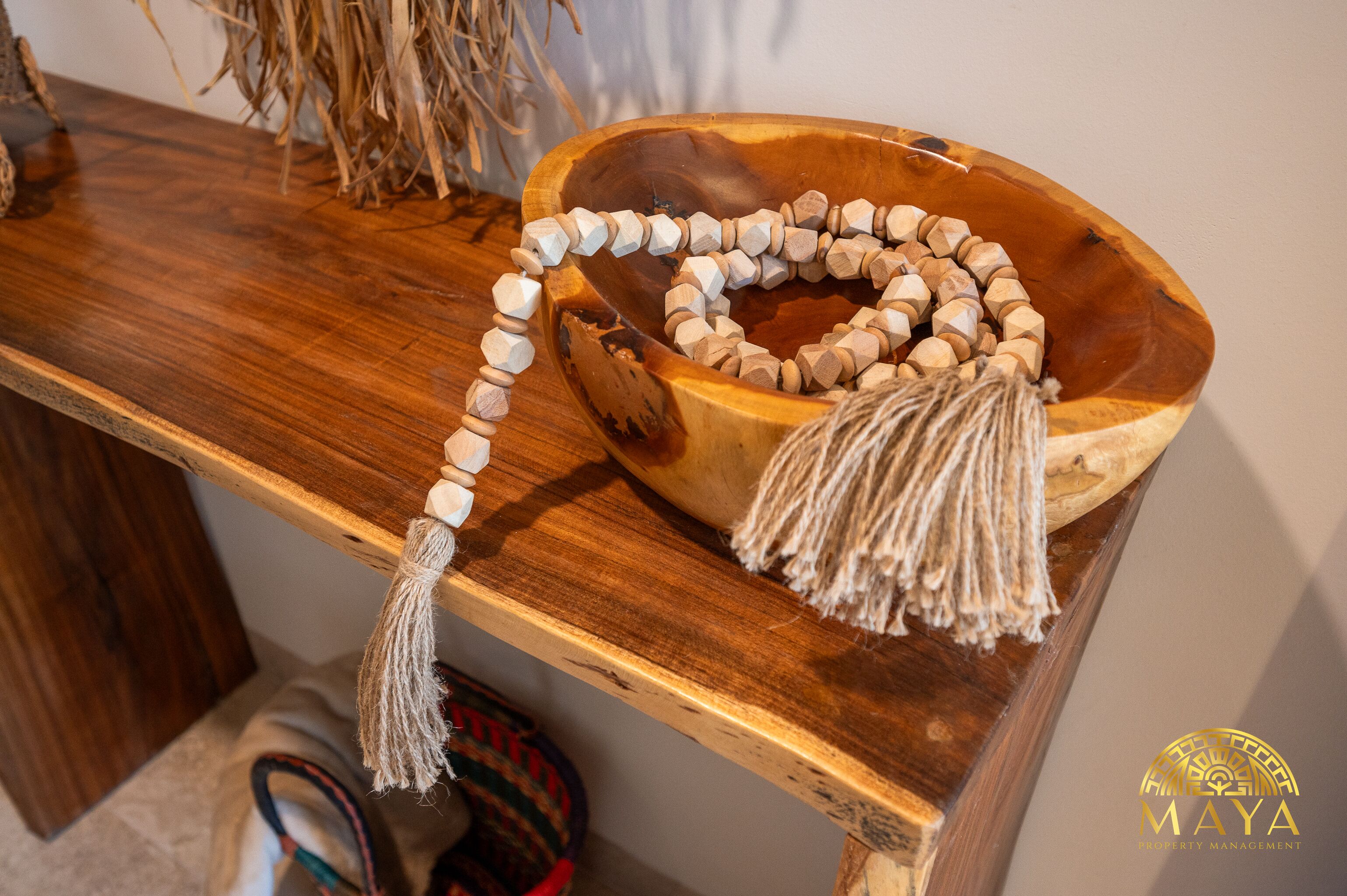 Un cuenco de madera con un collar de cuentas y una borla sobre una mesa de madera.