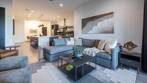 A modern living room with a grey sofa, a coffee table, and a dining area in the background. - Residence 2: The Villas At Troon North (Scottsdale)