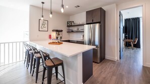 A modern kitchen with a large island, bar stools, stainless steel appliances, pendant lighting, and a view to a balcony. - Residence 2: The Villas At Troon North (Scottsdale)