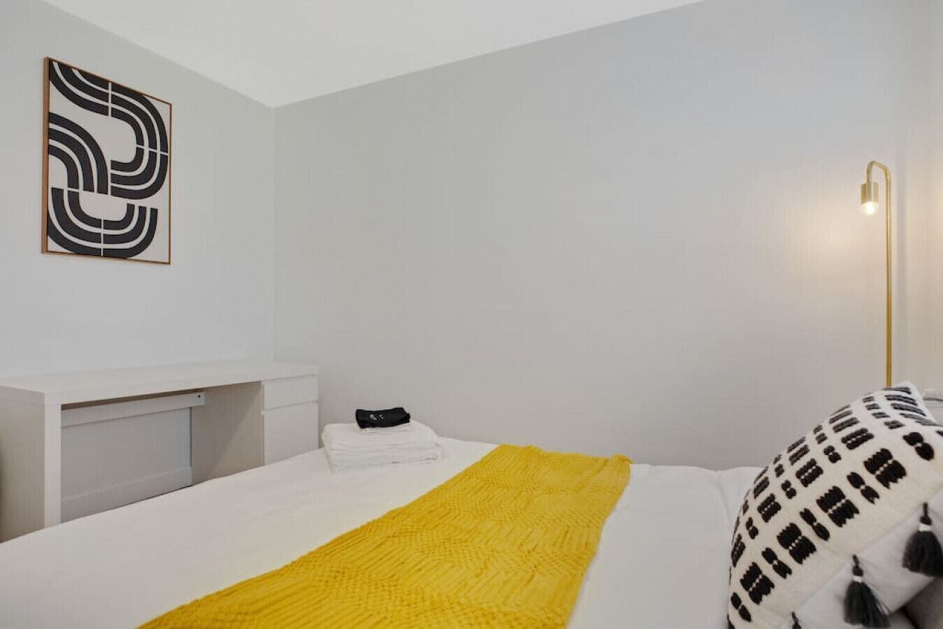 Une chambre à coucher moderne avec un lit, une table de chevet, une œuvre d’art accrochée au mur et une lampe sur pied.