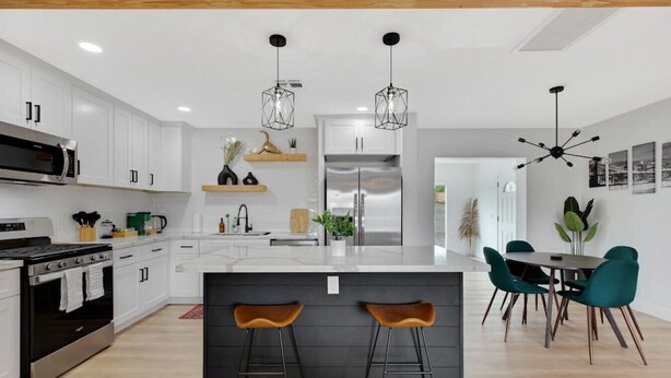 A modern kitchen with white cabinets, a central island with stools, a dining area with teal chairs, and pendant lighting. - Newly Renovated Home, 1 mi Downtown - 3 BR 2 Bath (Chandler)