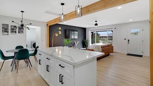 A modern kitchen with a central island, dining area with chairs, and a living room with a sofa and TV. - Newly Renovated Home, 1 mi Downtown - 3 BR 2 Bath (Chandler)