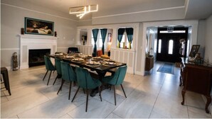 Une salle à manger avec une grande table dressée pour six personnes, des chaises de couleur turquoise, une cheminée et un lustre moderne.
