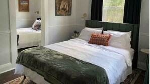 Une chambre à coucher avec un lit, une table de chevet, un miroir et une fenêtre avec des rideaux.
