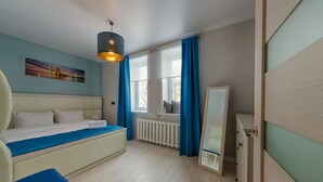 Un dormitorio con una cama, un radiador, una ventana con cortinas, una lámpara colgante y un espejo.