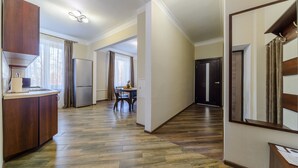 Un pasillo amplio con piso de madera, una zona de cocina con refrigerador y una mesa de comedor con sillas.