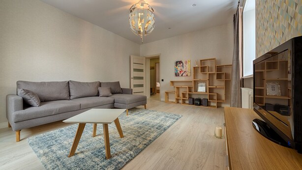 Una sala de estar moderna con un sofá seccional gris, una mesa de centro de madera, un tapete azul y blanco, estanterías de madera y un televisor plano grande.