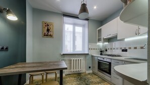 Una cocina moderna con armarios blancos, horno empotrado y comedor con mesa y sillas de madera.