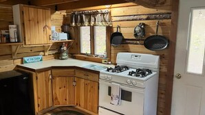 Une cuisine de cabane avec des murs en bois, un poêle, un réfrigérateur et un panneau indiquant les règles à respecter dans la cabane.