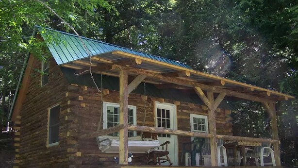 Une cabane rustique en rondins de bois, dotée d’un balcon, d’une terrasse en bois et d’un petit espace porche.