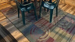 L’intérieur d’un chalet en bois accueillant, avec une table ronde en bois, quatre chaises vertes, un luminaire suspendu et deux fenêtres avec des rideaux.