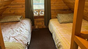 Une chambre mansardée chaleureuse avec deux lits, une fenêtre avec des rideaux et un ventilateur.