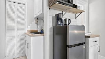 Une cuisine compacte équipée d’un réfrigérateur en acier inoxydable, d’un four à micro-ondes et d’une machine à café posés sur le plan de travail.