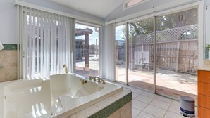 Un baño espacioso con una bañera grande, puertas de vidrio correderas que dan a un jardín y un mueble de madera.